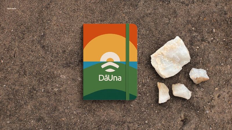 Caderno com a capa da DāUna, sobre solo arenoso e pedras de quartzo